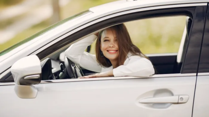 Smiling woman resting her elbow on the open window of a white car