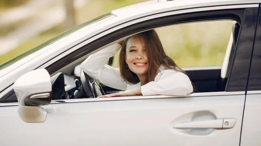 Smiling woman resting her elbow on the open window of a white car