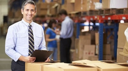 Business owner holding a clipboard standing next to inventory boxes in a warehouse