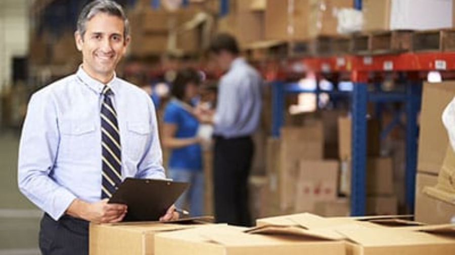 Business owner holding a clipboard standing next to inventory boxes in a warehouse