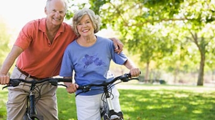 Senior couple standing outdoors in a park holding their bicycles and smiling