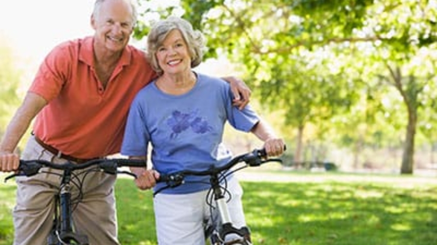 Senior couple standing outdoors in a park holding their bicycles and smiling