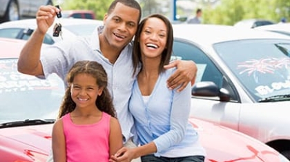 Happy family standing in front of a car holding up car keys at a dealership