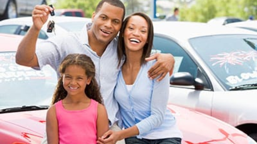 Happy family standing in front of a car holding up car keys at a dealership