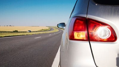 Rear taillight of a silver car parked on the shoulder of an open highway