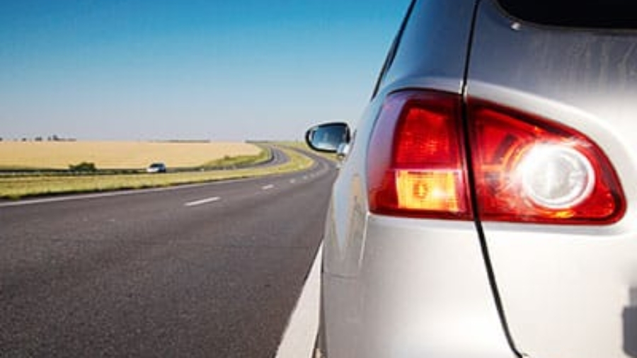 Rear taillight of a silver car parked on the shoulder of an open highway