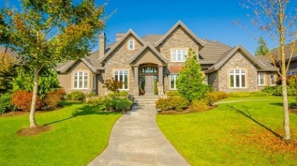 Large stone craftsman house with a manicured front lawn and walkway during early fall