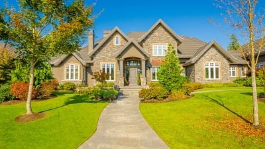 Large stone craftsman house with a manicured front lawn and walkway during early fall