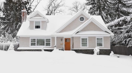 Residential house covered in deep snow and ice surrounded by snow-covered trees