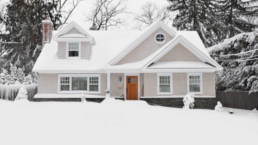 Residential house covered in deep snow and ice surrounded by snow-covered trees