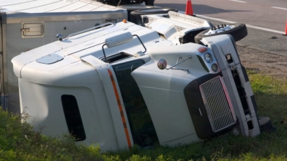 White semi-truck and trailer lying turned over on its side off the road following an accident