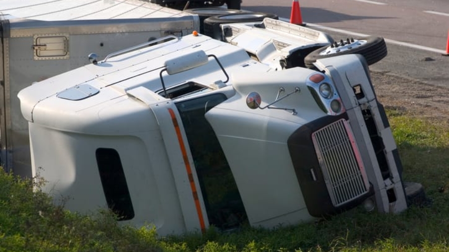 White semi-truck and trailer lying turned over on its side off the road following an accident
