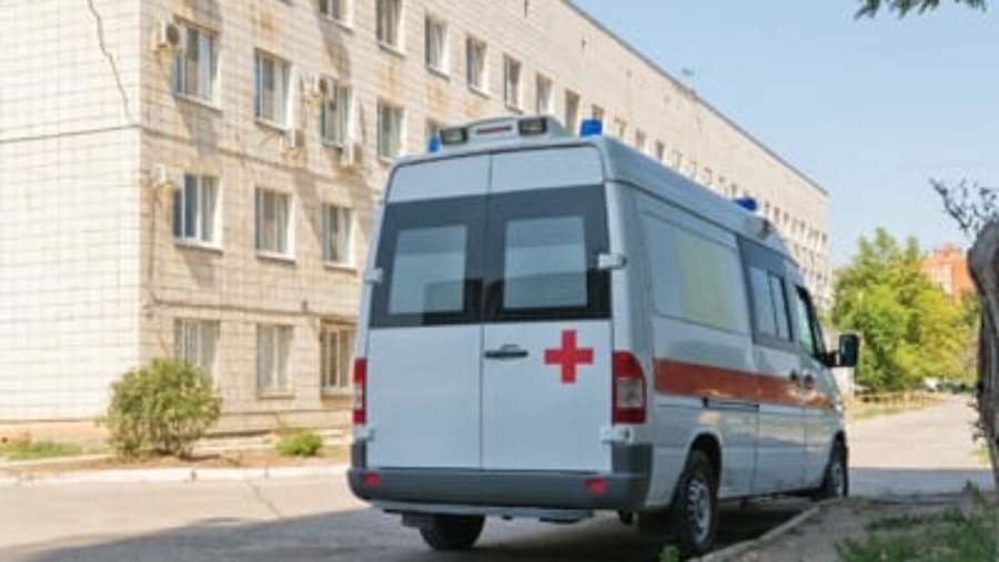 White non-emergency medical transportation van with a red cross logo parked outside a building