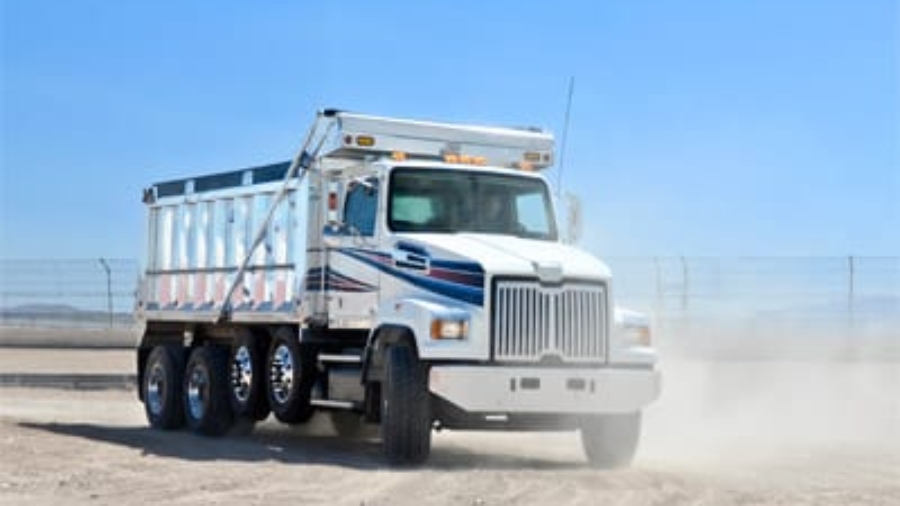 Large white dump truck driving on a dusty gravel construction site road