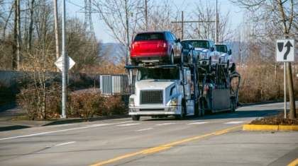 Large car carrier trailer truck loaded with multiple passenger vehicles driving on a road