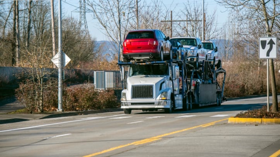 Large car carrier trailer truck loaded with multiple passenger vehicles driving on a road
