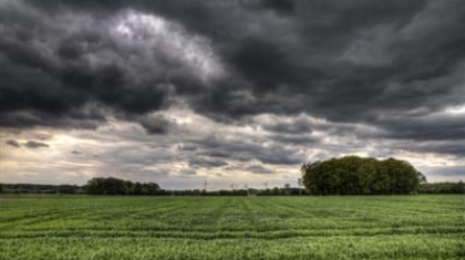 Dark storm clouds gathering above a green grassy field and distant tree line