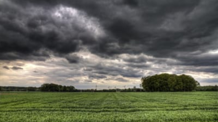 Dark storm clouds gathering above a green grassy field and distant tree line