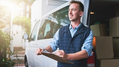 Delivery courier holding a clipboard and standing next to an open cargo van filled with delivery boxes