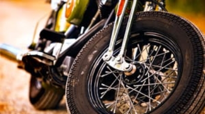 Close-up shot of the front wheel, spokes, and exhaust pipe of a parked motorcycle