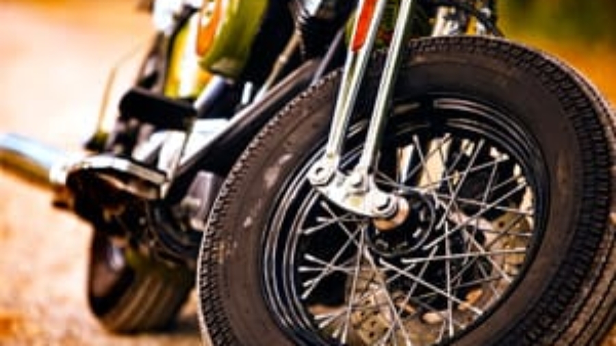 Close-up shot of the front wheel, spokes, and exhaust pipe of a parked motorcycle