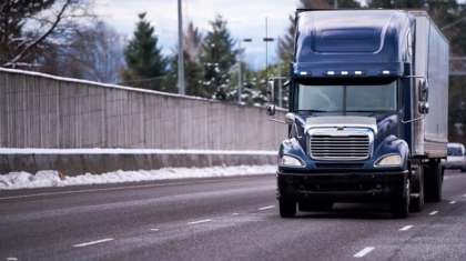 Blue semi-truck driving on a highway lined with snow during winter