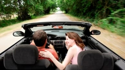 Couple driving down a tree-lined road in a convertible car