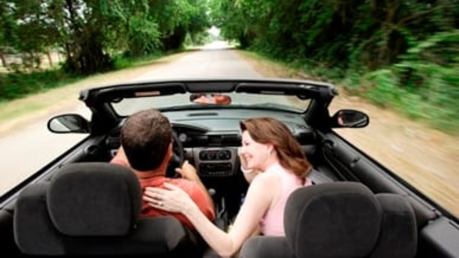Couple driving down a tree-lined road in a convertible car