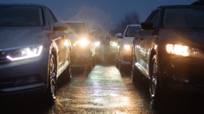 Cars driving on a wet road at dusk with bright headlights illuminated
