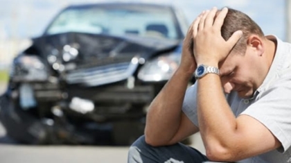 Stressed driver sitting with hands on his head in front of a damaged car after an accident