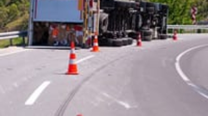 Overturned commercial semi-truck flipped on its side along a highway curve lined with traffic cones