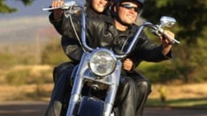 Two helmeted motorcycle riders wearing protective jackets riding a cruiser motorcycle on an open road