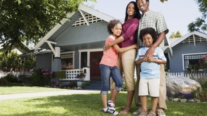 Family of four standing on the lawn outside their suburban blue house