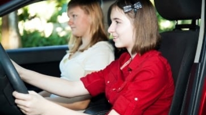 Two teenage girls smiling inside a car while one holds the steering wheel