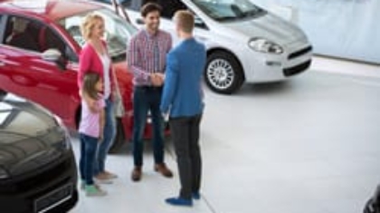 Family talking with a car dealership salesperson in a showroom with compact cars