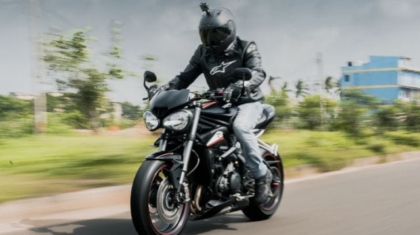 Motorcycle rider wearing a dark helmet and protective jacket riding a black sport bike down a road