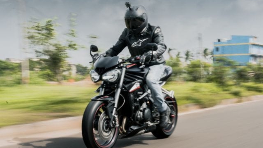 Motorcycle rider wearing a dark helmet and protective jacket riding a black sport bike down a road