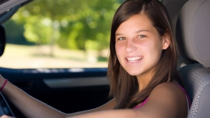 Smiling teenage girl sitting in the driver seat holding the steering wheel