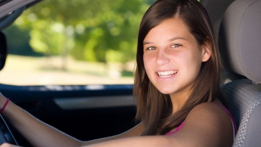 Smiling teenage girl sitting in the driver seat holding the steering wheel