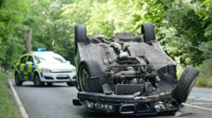 Overturned vehicle lying on its roof on a road with a police car approaching in the background