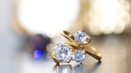 Gold ring with three prominent diamonds displayed against a bokeh background