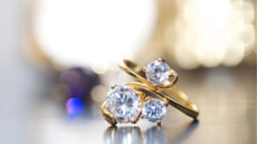 Gold ring with three prominent diamonds displayed against a bokeh background