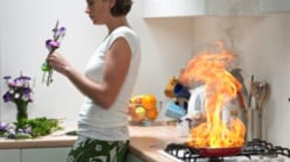 Woman arranging flowers in a kitchen while a cooking pan on the stove catches fire