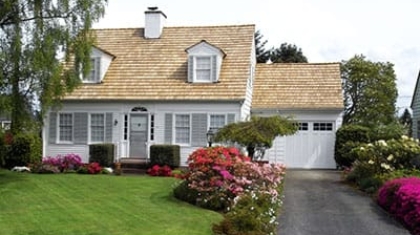 Two-story white residential home with a garage, green lawn, and blooming flower beds