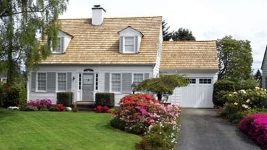Two-story white residential home with a garage, green lawn, and blooming flower beds