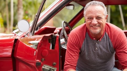 Smiling senior man leaning out of the open driver door of a classic red car