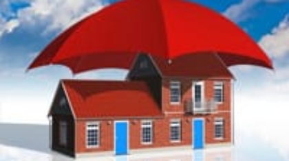 Model house protected under a large open red umbrella against a blue sky