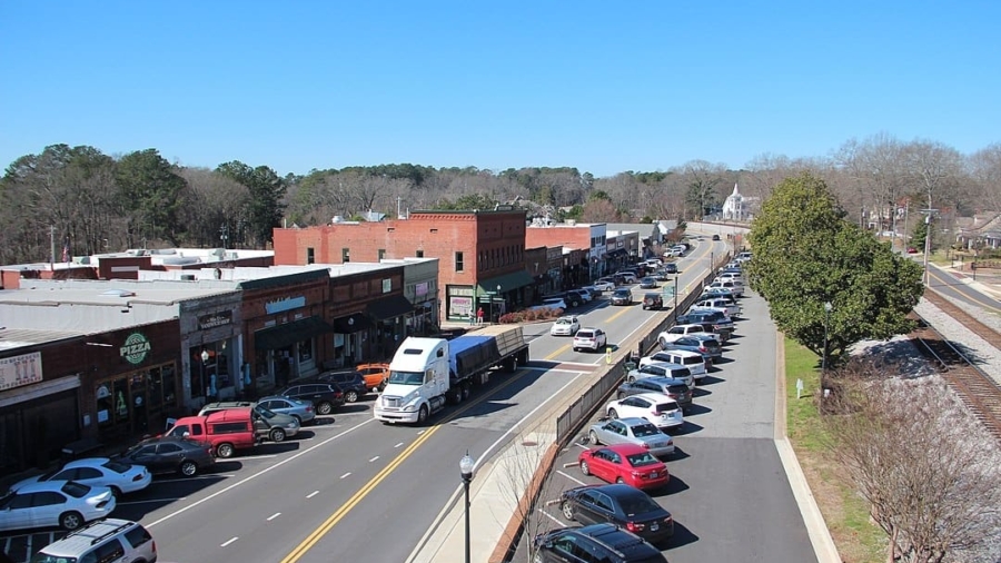 Elevated view of a commercial town street filled with traffic, parked cars, and storefronts along a railway track