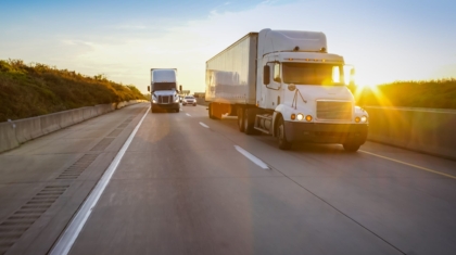 White semi tractor-trailer driving on an open highway during a sunny evening