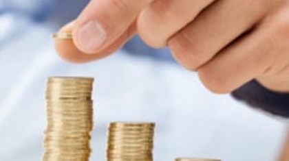 Hand placing a coin on top of small growing stacks of gold coins
